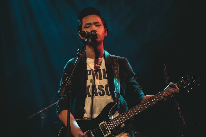 Musician playing electric guitar and singing on stage under spotlight.